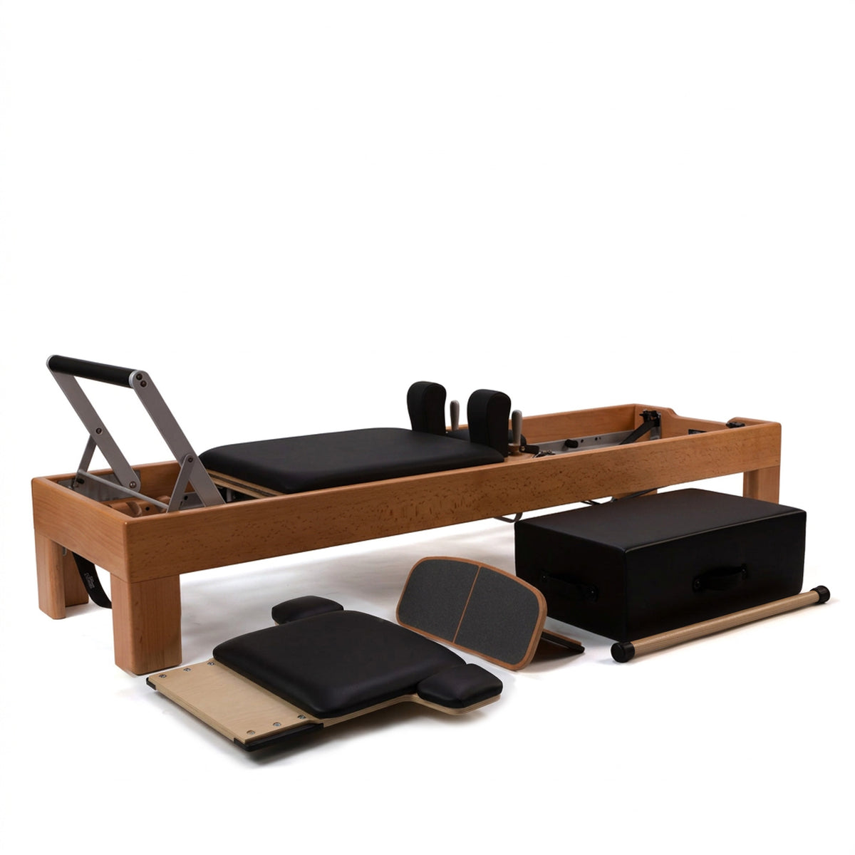 A wooden Pilates reformer machine with black padded cushioning, shown with several accessories including a black box, foot platform, and dancer jumpboard on a clean white background.
