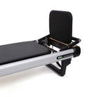 Close-up of a Peak Pilates MVe reformer showing the black padded footrest, backrest, metal frame on a white background.