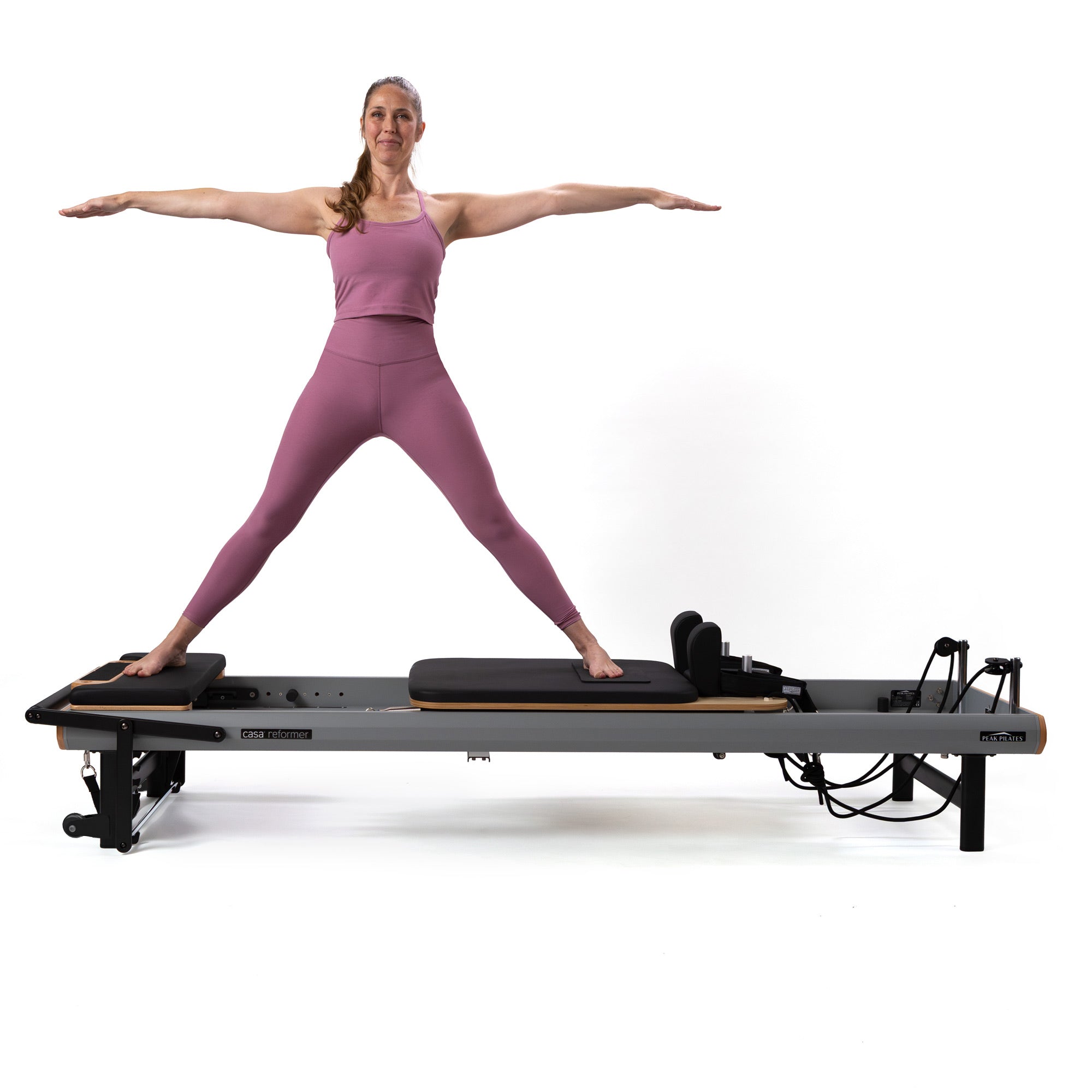 Woman in pink workout attire standing on a casa reformer Pilates machine by Peak Pilates