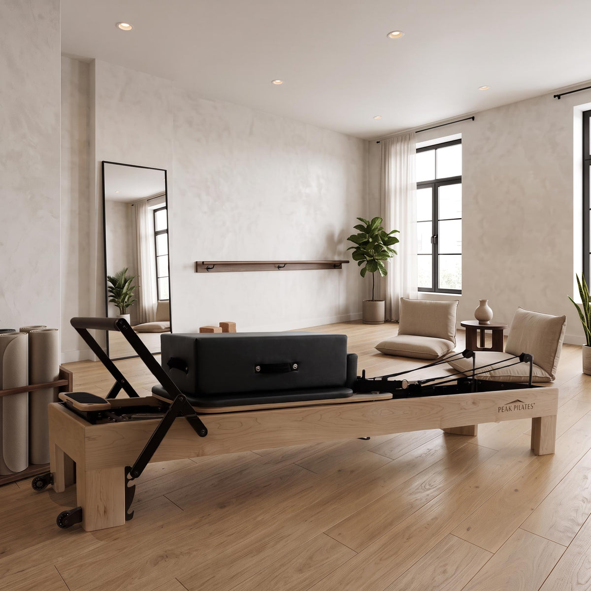 A Peak Pilates Arbor reformer with a natural wood frame and black carriage, set in a bright, modern studio with light wood floors, textured walls, and a large mirror.