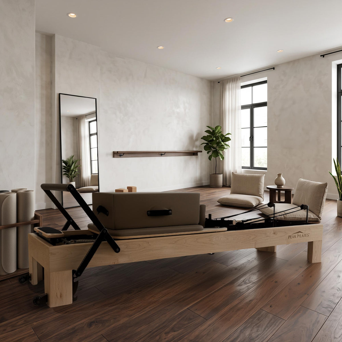 A Peak Pilates Arbor reformer with a natural wood frame and mocha long/short box and upholstery on the  carriage, set in a bright, modern studio with light wood floors, textured walls, and a large mirror.