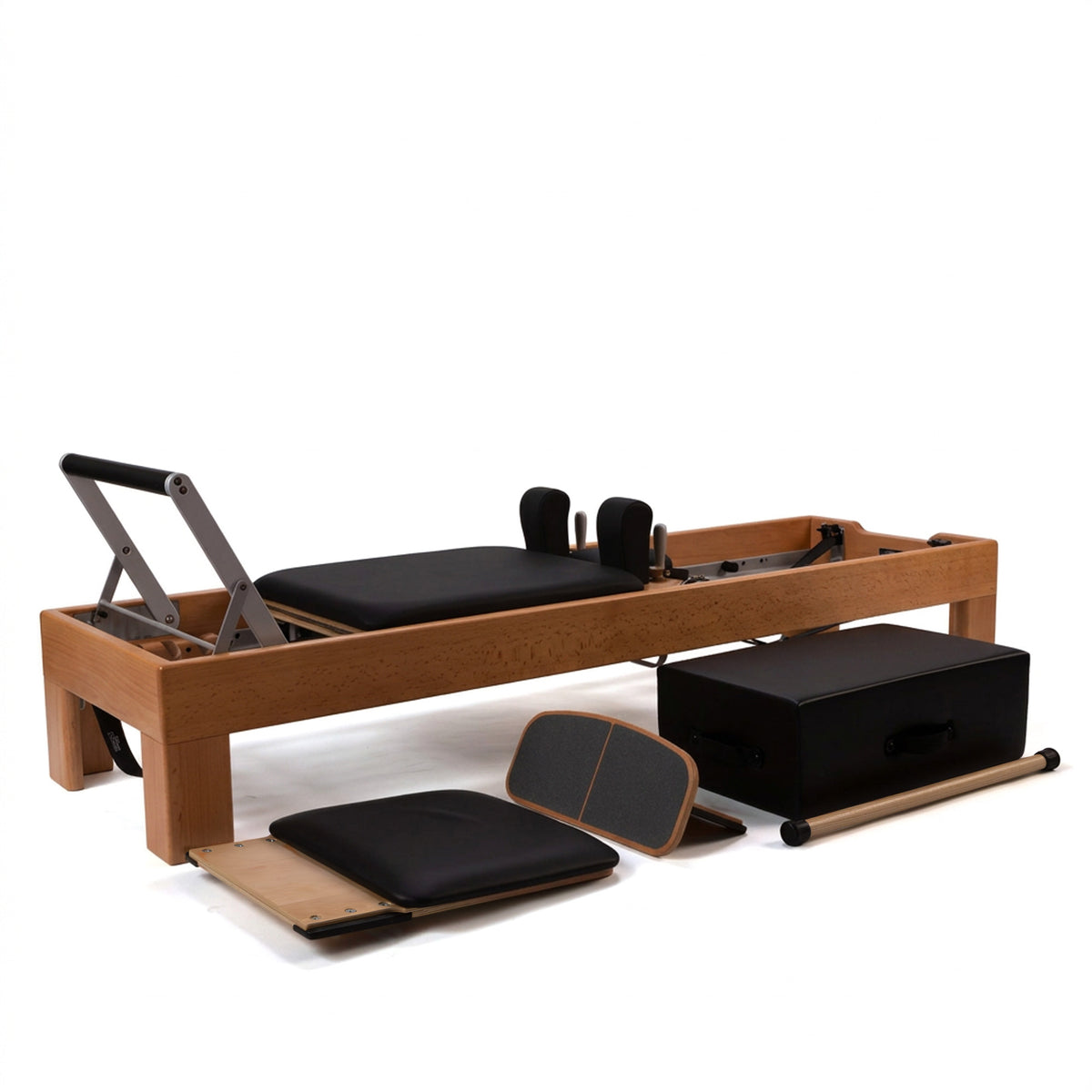 A wooden Artistry Pilates reformer with black padded seat, footrest, and straps, long/short box, extended foot platform and jump board shown on a clean white studio background.