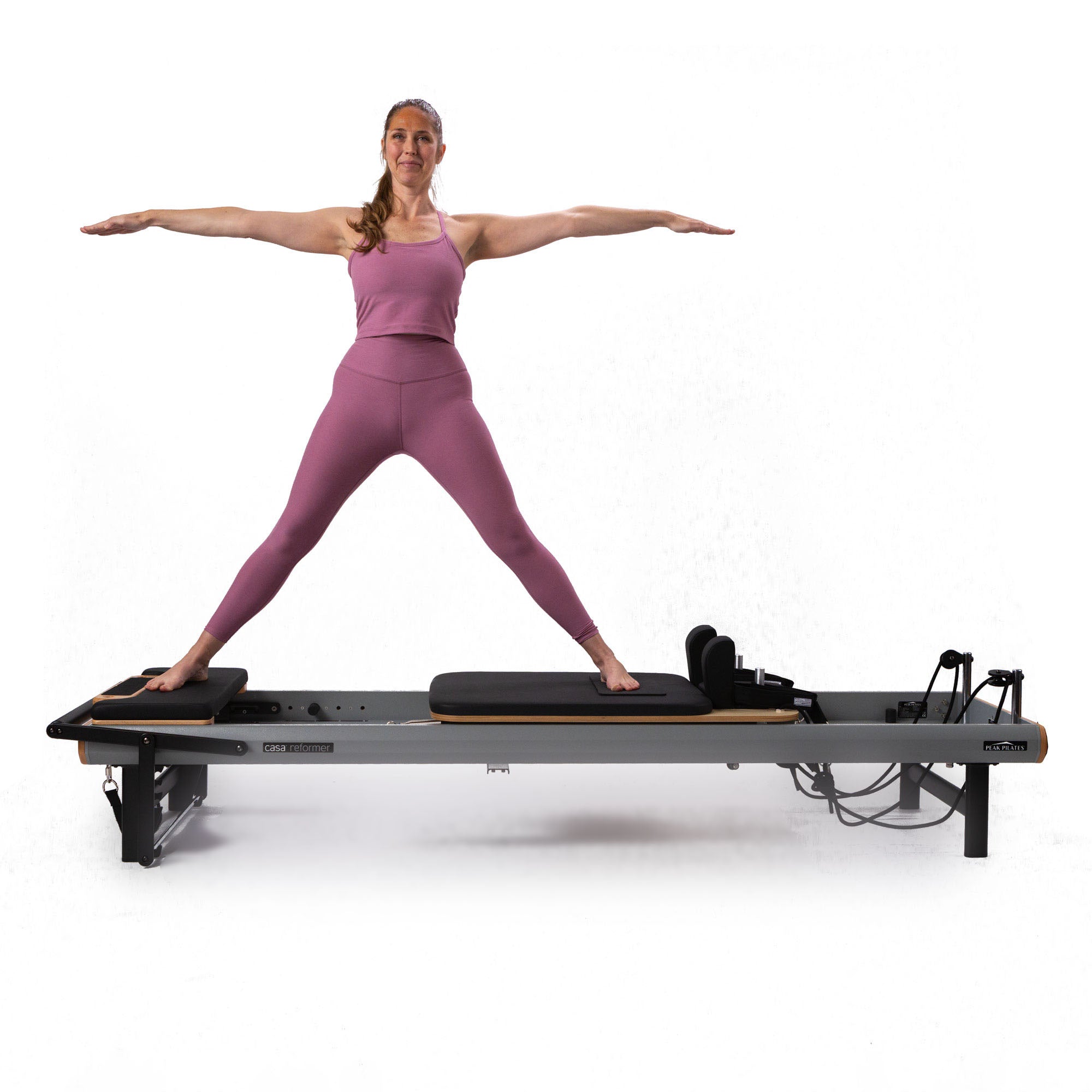 Woman in pink workout attire standing on a casa reformer Pilates machine by Peak Pilates
